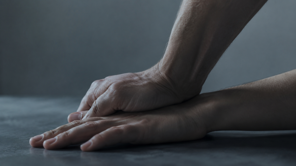 Significato di sadico: due mani in primo piano, una che preme sull’altra con tensione controllata, metafora di dominio e dislivello di potere
