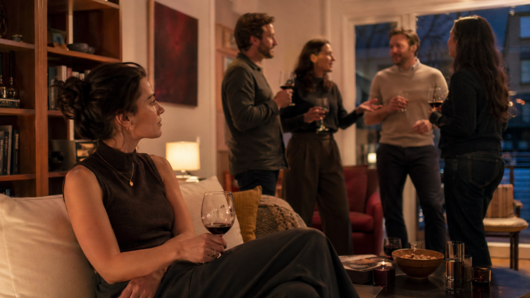 Persona introversa in disparte durante una festa, mentre il gruppo conversa animatamente: scena tipica di come gli introversi vivono i contesti sociali